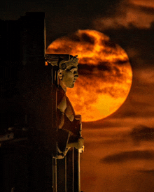 a statue of a man with wings is standing in front of a full moon
