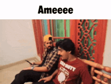 a man in a call of duty shirt sits next to another man on a couch
