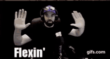 a man with a beard wearing headphones and a hat is making a funny face with his hands .