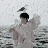 a seagull sits on a man 's head in front of a window with rain drops