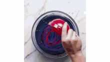 a person is holding a red ball in a bowl of blue and red dye .