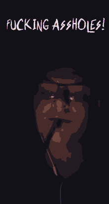 a man wearing glasses is smoking a cigarette with the words fucking assholes written above him .