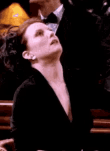 a woman in a black jacket is looking up at a man in a tuxedo in a dark room .
