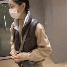 a woman wearing a mask and a vest holds her hands together