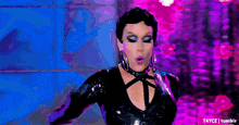 a woman in a black dress is blowing a kiss on a pink background .
