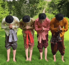 a group of people in traditional clothes are kneeling in the grass and praying .