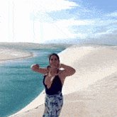 a woman in a black tank top is standing on a sand dune next to a body of water