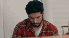 a man with a beard is sitting at a table looking down at something .