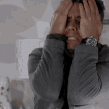 a man covering his face with his hands and wearing a watch that says the time is 4:20