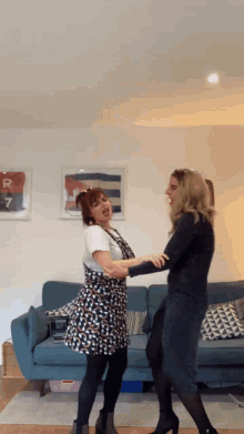 two women are dancing in front of a blue couch with a picture on the wall that says r