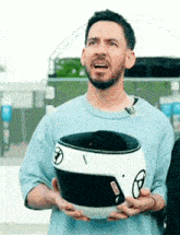 a man in a blue shirt is holding a white and black helmet .
