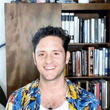 a man in a hawaiian shirt is smiling in front of a bookshelf filled with books .