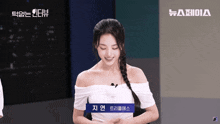 a woman wearing a white off the shoulder top with a blue label that says " 지연 "