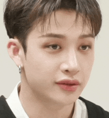a close up of a young man 's face with a white shirt and earrings .