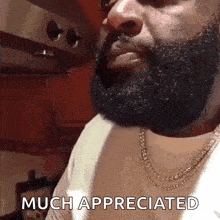 a man with a beard and a necklace is smoking a cigarette in a kitchen .