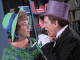 a man in a purple top hat talks to a woman in a green and blue dress