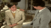 a man in a suit is talking to another man in a gray suit