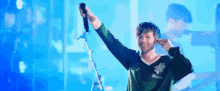 a man is singing into a microphone on a stage while wearing a green shirt .