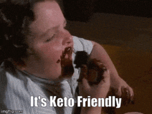 a man is eating a chocolate donut with the words " it 's keto friendly " above him