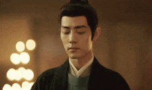 a man with his eyes closed and a bun on his head is standing in a room .