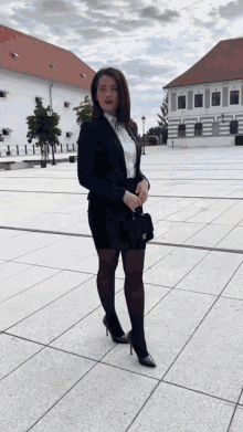a woman in a black suit and white shirt is standing on a sidewalk