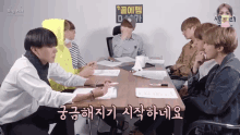 a group of young men are sitting around a table with papers on it and a sign that says big hit