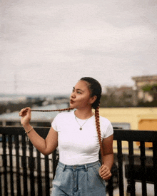 a woman wearing a white t-shirt and denim shorts is holding a braid
