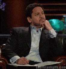 a man in a suit is sitting in a chair with a sharktankglis.com watermark