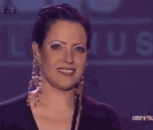 a woman wearing a black shirt and earrings is smiling in front of a sign that says louis