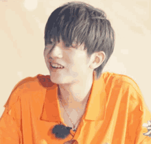 a close up of a young man wearing an orange shirt and smiling .