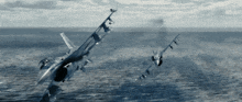 two fighter jets are flying over the ocean and one has smoke coming out of its tail