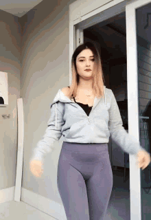 a woman wearing purple leggings and a grey jacket is standing in front of a glass door