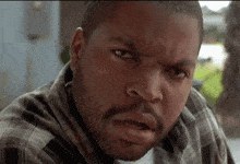 a man in a plaid shirt is looking at the camera with a serious look on his face