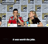a man and a woman are sitting at a table talking into microphones at a convention .