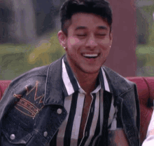 a young man wearing a striped shirt and a denim jacket is smiling