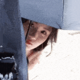 a woman is holding an umbrella over her head and peeking out from behind it .