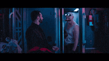 a man with a beard and goggles is talking to another man in a dark room