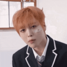 a young man with orange hair is wearing a school uniform and tie and has a bandage on his face .