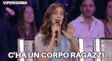 a woman is holding a microphone in front of a crowd and saying c 'ha un corpo ragazzi .