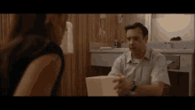 a man is talking to a woman in a bathroom while holding a box .