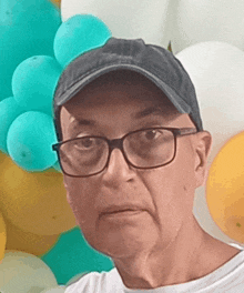 a man wearing glasses and a hat is standing in front of a bunch of balloons