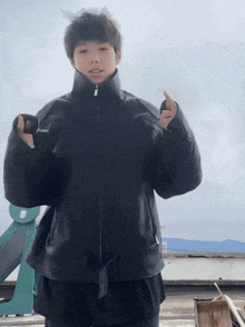 a young man in a black jacket is giving a thumbs up sign