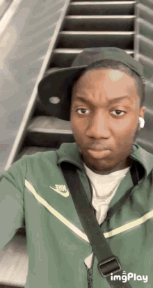 a man wearing a green nike jacket and a black hat takes a selfie