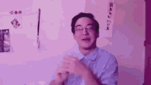 a man wearing glasses and a blue shirt is clapping his hands in front of a purple wall .