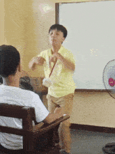 a boy in a yellow shirt stands in front of a white board with a fan on it