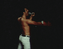 a shirtless man singing into a microphone on stage