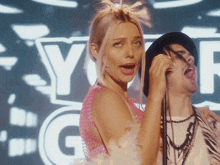 a woman in a pink dress sings into a microphone in front of a sign that says y-g-r