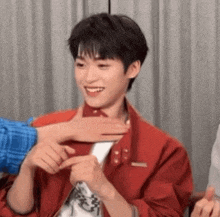 a young man in a red jacket is being touched by someone .