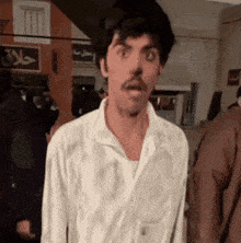 a man in a white shirt with a mustache looks surprised