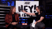 two men are sitting in front of a sign that says " hey "